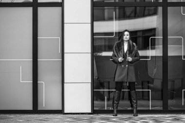 Bir ofis binasının yakınındaki zarif giyimli bir iş kadınının siyah beyaz portresi.