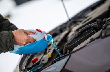 Sürücü, arabanın deposundaki mavi, donmayan ön cam temizleme sıvısını dolduruyor.