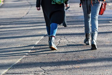 İnsanlar güneşli bir günde asfalt kaldırımda yürüyorlar. Bacakları gölgeli.