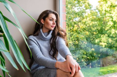 Genç, şehvetli, uzun saçlı esmer kadın evdeki pencere eşiğinde oturuyor.