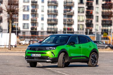 Riga, Letonya - 26 Mart 2021: yeşil elektrikli araç Opel Mokka-e kentsel yerleşim alanının arka planındaki otoparkta