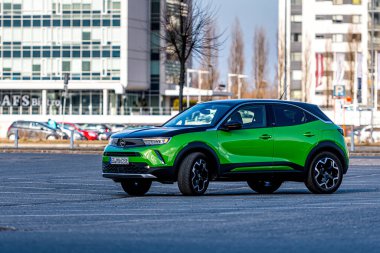 Riga, Letonya - 26 Mart 2021: yeşil elektrikli araç Opel Mokka-e kentsel yerleşim alanının arka planındaki otoparkta