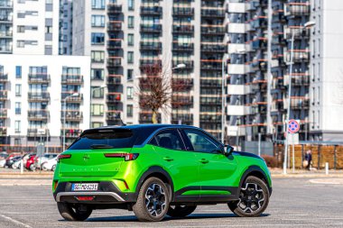 Riga, Letonya - 26 Mart 2021: yeşil elektrikli araç Opel Mokka-e kentsel yerleşim alanının arka planındaki otoparkta