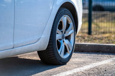 Caddenin kenarına park etmiş beyaz bir aracın arka tekerine yakın plan.