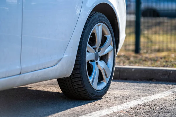 Caddenin kenarına park etmiş beyaz bir aracın arka tekerine yakın plan.