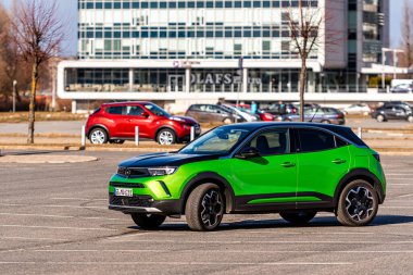 Riga, Letonya - 26 Mart 2021: yeşil elektrikli araç Opel Mokka-e kentsel yerleşim alanının arka planındaki otoparkta