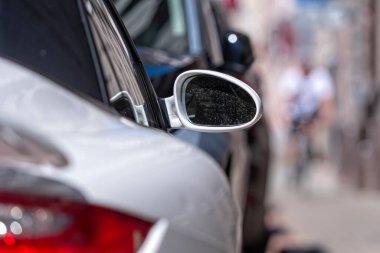 Caddenin kenarına park edilmiş sıra sıra araba, ön planda beyaz spor araba, detaylara yakın çekim.