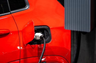 Şarj kablosunun fişi bir elektrikli arabaya takılı, istasyonda bir elektrikli arabayı şarj ediyor.