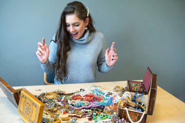 Masada bir sürü mücevherle oturan ince esmer, farklı mücevherler seçiyor ve deniyor.