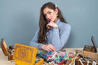 Masada bir sürü mücevherle oturan ince esmer, farklı mücevherler seçiyor ve deniyor.