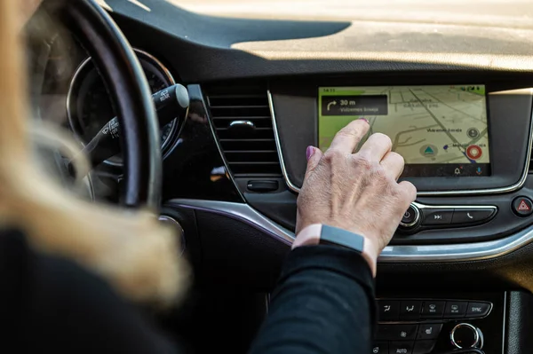 woman driving car, presses finger on touch screen, using car navigation system
