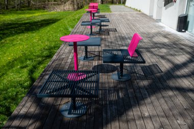 Güneşli bir günde terasta renkli metal banklar ve masalar