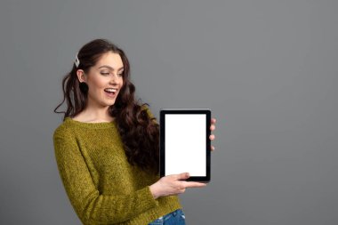 duygusal genç kadın gri arkaplanda izole edilmiş, boş dokunmatik ekranlı tablet bilgisayarını gösteriyor