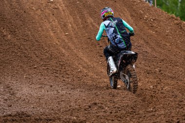 Dobele, Letonya, 18 Haziran 2022: Toprak yol ve tepe arazileri boyunca hareket halindeki bir grup motokros sürücüsü, arkadan görülüyor