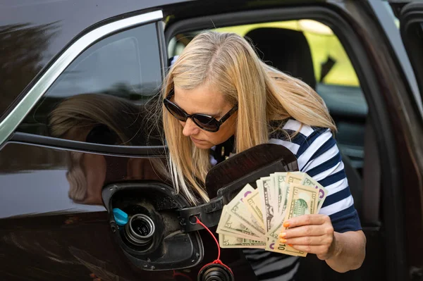 worried woman with dollar cash looking at the open car tank, the concept of rising fuel prices