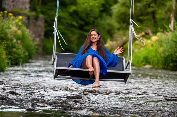 a smiling young woman swings on a rope swing across a fast-flowing river