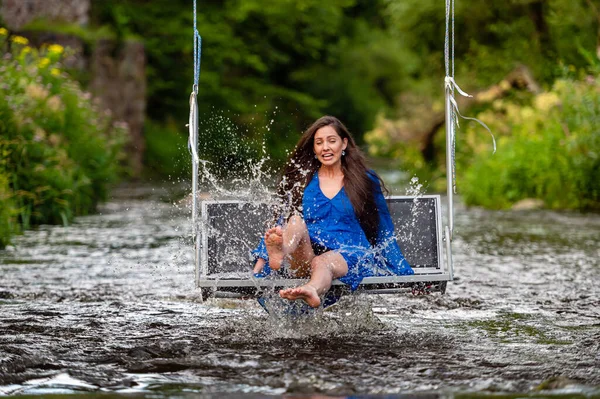 a smiling young woman swings on a rope swing across a fast-flowing river