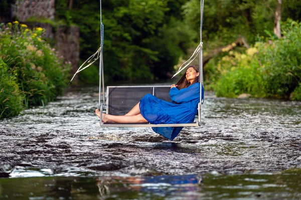 a smiling young woman swings on a rope swing across a fast-flowing river