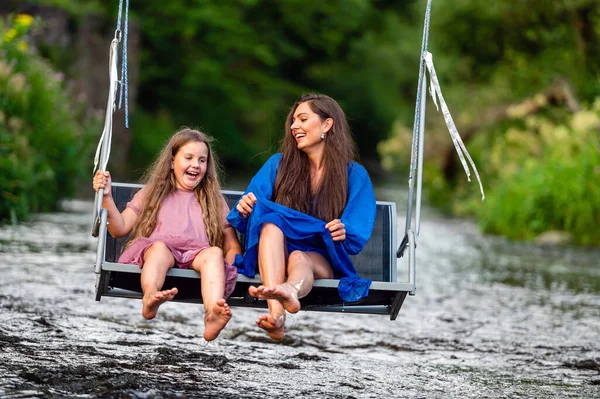 laughing woman and a young girl swing over a fast-flowing river, splashing the water with their feet