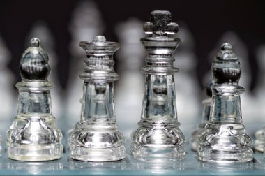 clear glass, transparent chess pieces on a checkerboard, selective focus, closeup, isolated on black