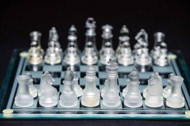 clear glass, transparent chess pieces on a checkerboard, selective focus, closeup, isolated on black
