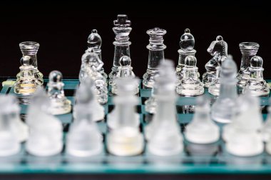 clear glass, transparent chess pieces on a checkerboard, selective focus, closeup, isolated on black
