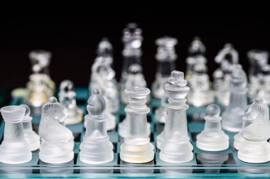 clear glass, transparent chess pieces on a checkerboard, selective focus, closeup, isolated on black