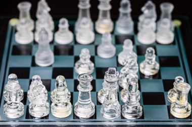 clear glass, transparent chess pieces on a checkerboard, selective focus, closeup, isolated on black
