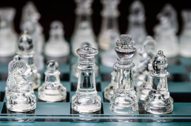 clear glass, transparent chess pieces on a checkerboard, selective focus, closeup, isolated on black
