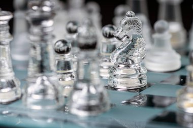 transparent glass chess on dark background, selective focus on knight piece, close-up