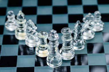 clear glass chess figures arranged in a row reflecting in glass chessboard. Isolated on black