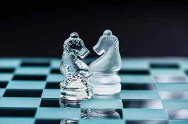 two opponent glass chess knights on a glass chess board, black background, copy space