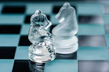 two opponent glass chess knights on a glass chess board, black background, copy space