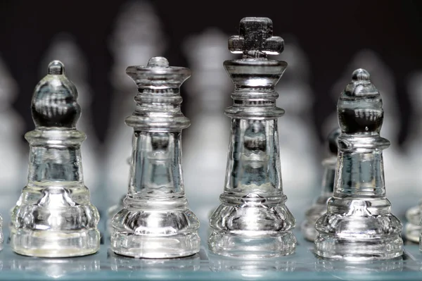 clear glass, transparent chess pieces on a checkerboard, selective focus, closeup, isolated on black