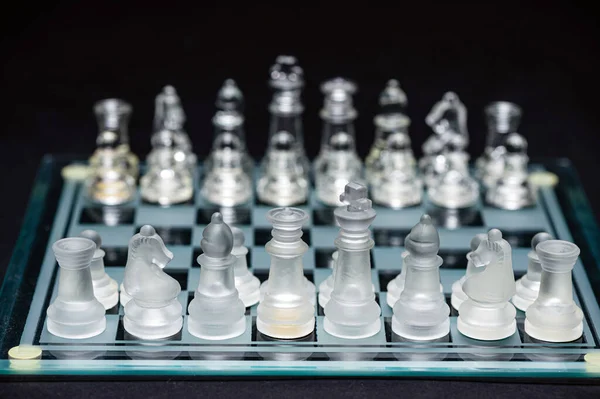 clear glass, transparent chess pieces on a checkerboard, selective focus, closeup, isolated on black