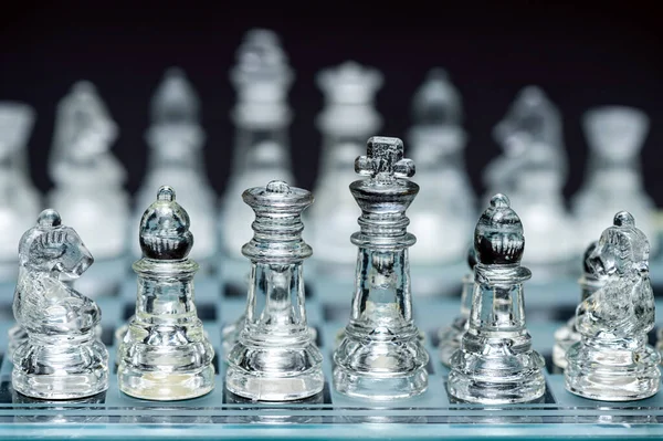 clear glass, transparent chess pieces on a checkerboard, selective focus, closeup, isolated on black
