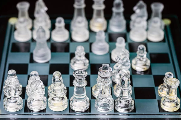 clear glass, transparent chess pieces on a checkerboard, selective focus, closeup, isolated on black