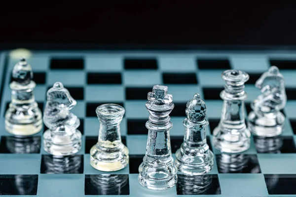 clear glass chess figures arranged in a row reflecting in glass chessboard. Isolated on black