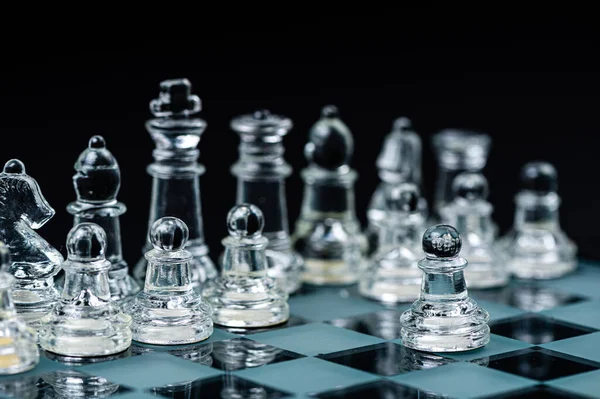 clear glass, transparent chess pieces on a checkerboard, selective focus, closeup, isolated on black