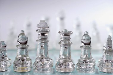 clear glass, transparent chess pieces on a checkerboard, selective focus, closeup, isolated on light