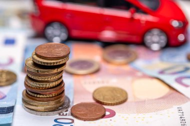 Tower with euro coins on the background of banknotes and red toy car, loan and insurance concept