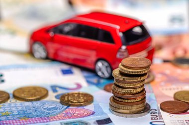 Tower with euro coins on the background of banknotes and red toy car, loan and insurance concept