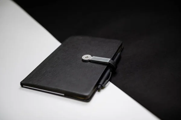 black planner or notebook with pen on two-color black and white background, mockup, copy space