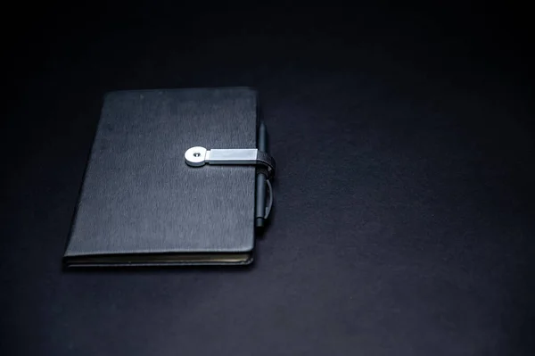 black planner or notebook with pen isolated on black background, mockup, copy space, close-up