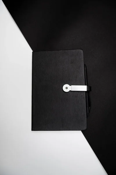 black planner or notebook with pen on two-color black and white background, mockup, copy space