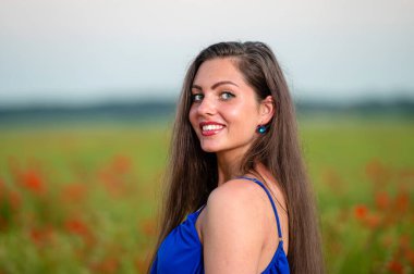 Akşam vakti gelincik tarlasında uzun saçlı zarif genç bir kadının portresi.