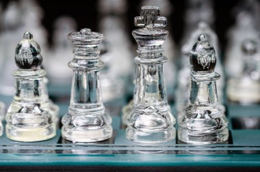 clear glass, transparent chess pieces on a checkerboard, selective focus, closeup, isolated on black