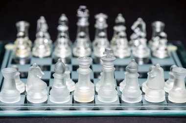 clear glass, transparent chess pieces on a checkerboard, selective focus, closeup, isolated on black