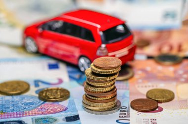 Tower with euro coins on the background of banknotes and red toy car, loan and insurance concept