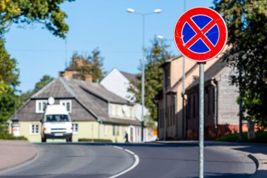 Önünde yol tabelası olan küçük bir kasaba caddesi manzarası ve arka planda trafiği dağıtan